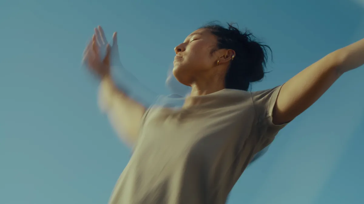 A dancer with arms flung wide against a clear blue sky.